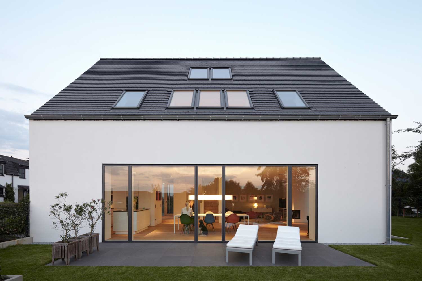 Architekturfotografie Lioba Schneider: Weisses Einfamilienhaus in Troisdorf. Große Flügeltüren aus Glas öffnen nach aussen auf die Terrasse bei Dämmerung.