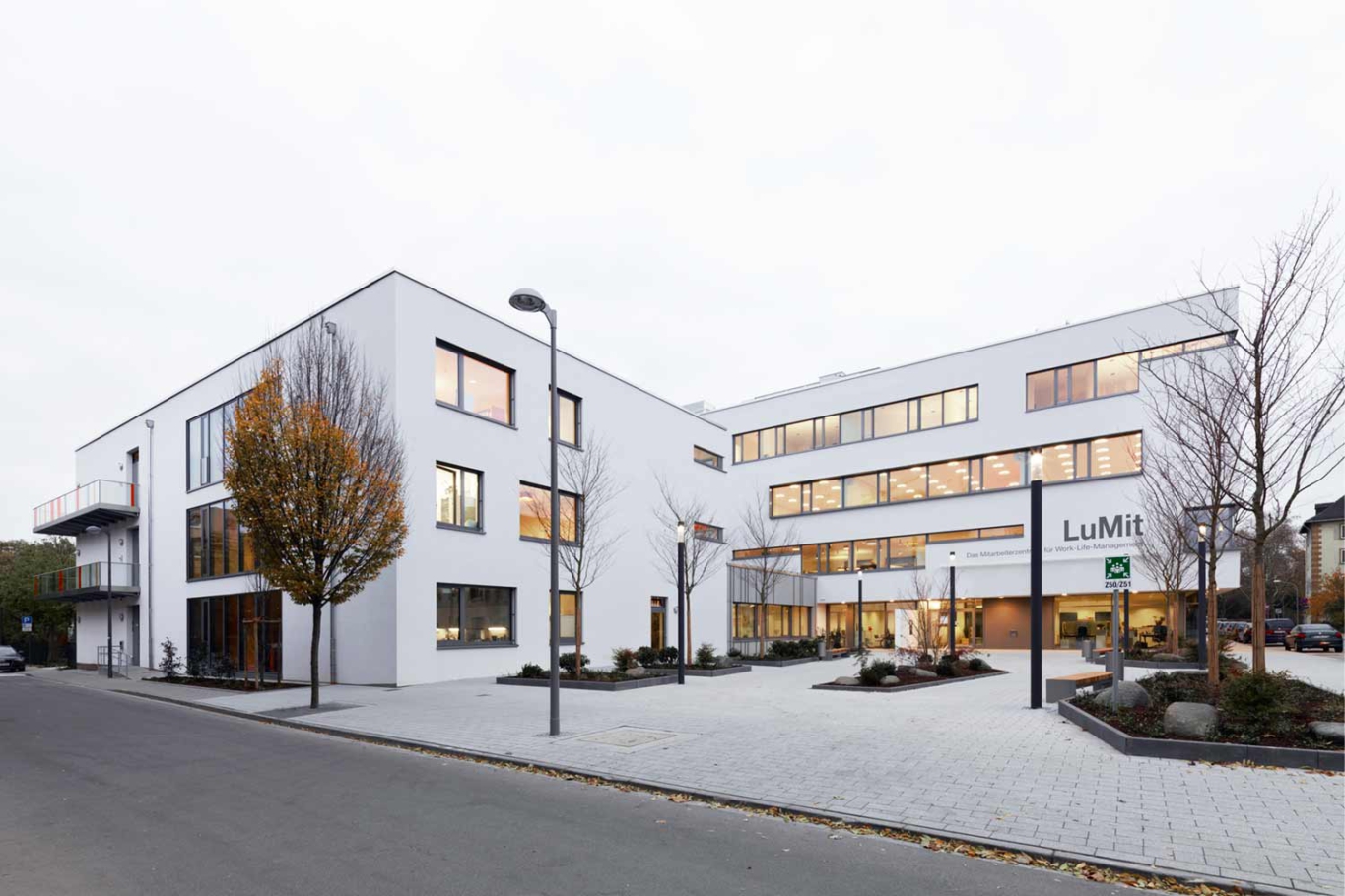 Architekturfotografie Lioba Schneider: Neubau des LUMIT-Gebäudes für BASF. Durchgehende Fensterbänder strukturieren den vierstöckigen weissen Baukörper. Ansicht von der Strasse bei Dämmerung.