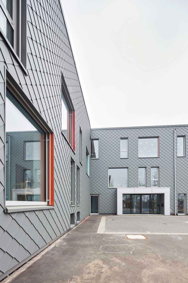 Architekturfotografie Lioba Schneider: Modern gelöste Sanierung und Erweiterung einer Förderschule in Alfter bei Bonn. Große uneregelmässige Fenster strukturieren die Fassade aus rautenförmigen Aluminiumschindeln.