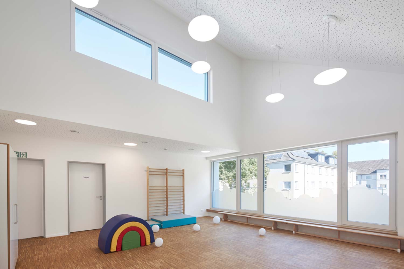 Lioba Schneider Architekturfotografie: In vier miteinander verbundenen Gebäuden mit Spitzgiebel wurde eine neue Kita untergebracht. Jedes Haus hat eine eigene sehr bunte Farbe, die Dächer sind im gleichen Farbton gehalten.