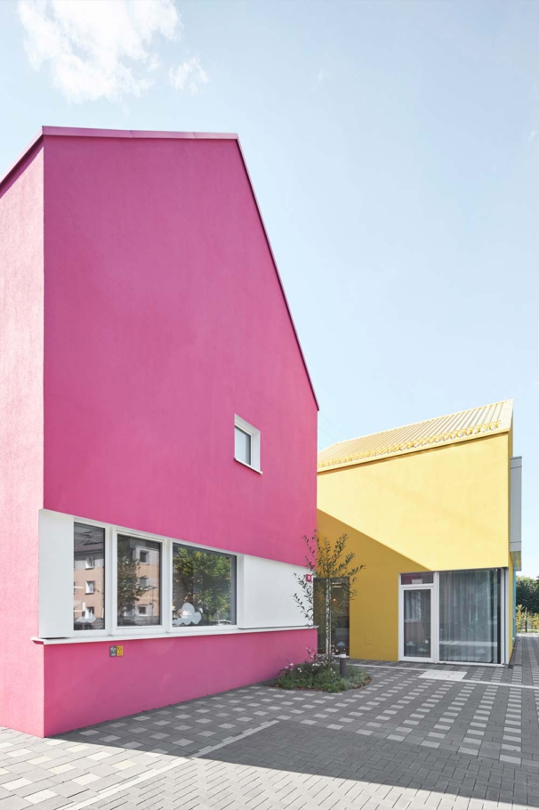 Lioba Schneider Architekturfotografie: In vier miteinander verbundenen Gebäuden mit Spitzgiebel wurde eine neue Kita untergebracht. Jedes Haus hat eine eigene sehr bunte Farbe, die Dächer sind im gleichen Farbton gehalten.