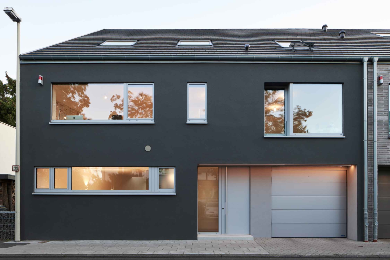 Architekturfotografie Lioba Schneider: Ein Doppeleinfamilienhaus in Bonn bei Dämmerung von der Strasse aus gesehen. Die Fassaden sind unterschiedlich gestaltet- anthrazitfarbener putz und einmal heller Klinker.