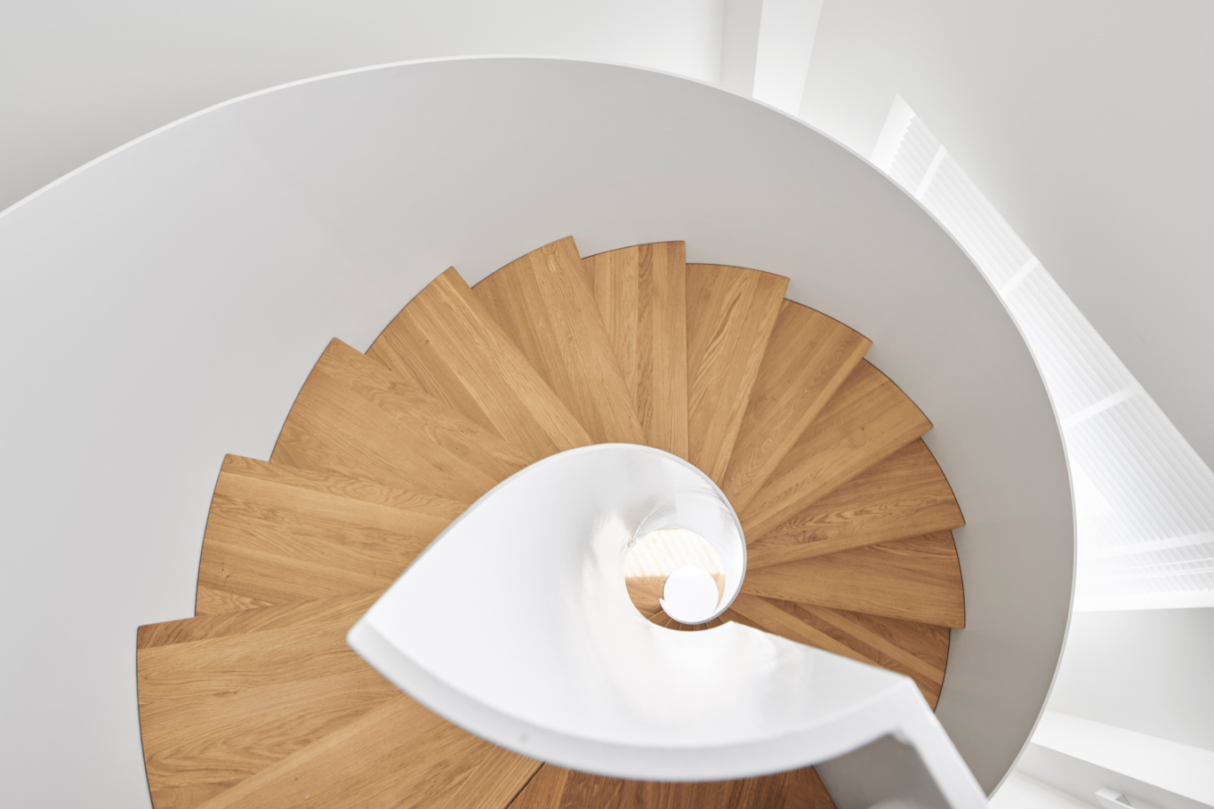 Architekturfotografie: Elegante Wendeltreppe von oben, Materialmix aus weissem Stahl und Stufen aus hellem Holz