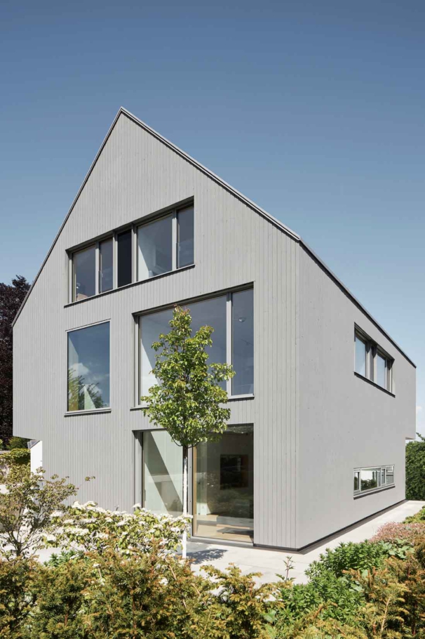 Architekturfotografin Lioba Schneider fotografiert im Auftrag von tr-architekten: Spitzgiebeliges graues Einfamilienhaus in Holzbauweise. Große Fenster lassen viel Licht ins Innere.