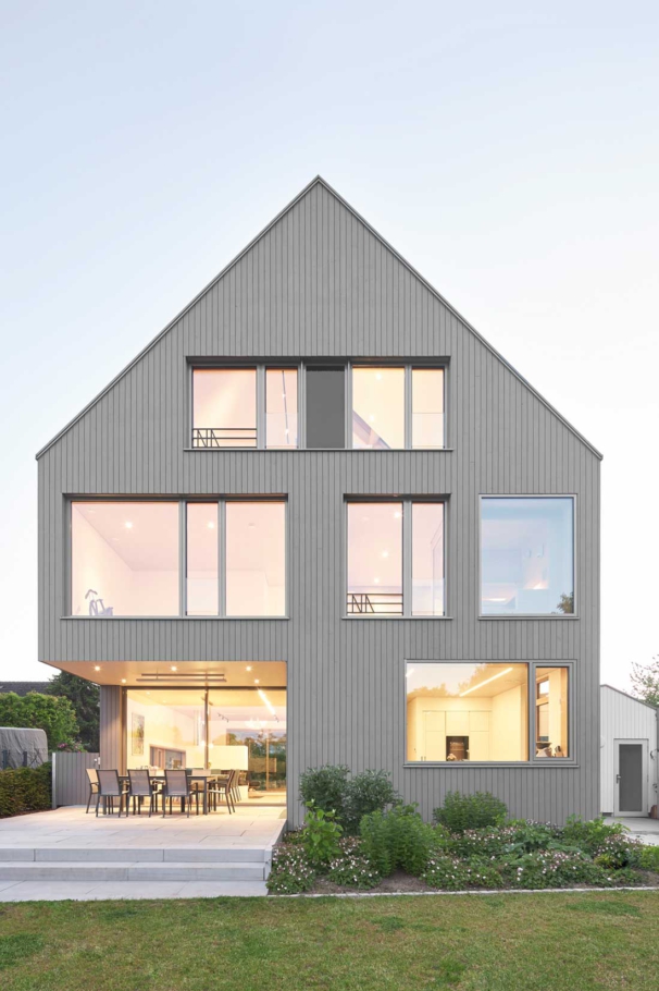 Architekturfotografin Lioba Schneider fotografiert im Auftrag von tr-architekten: Spitzgiebeliges graues Einfamilienhaus in Holzbauweise. Große Fenster lassen viel Licht ins Innere.