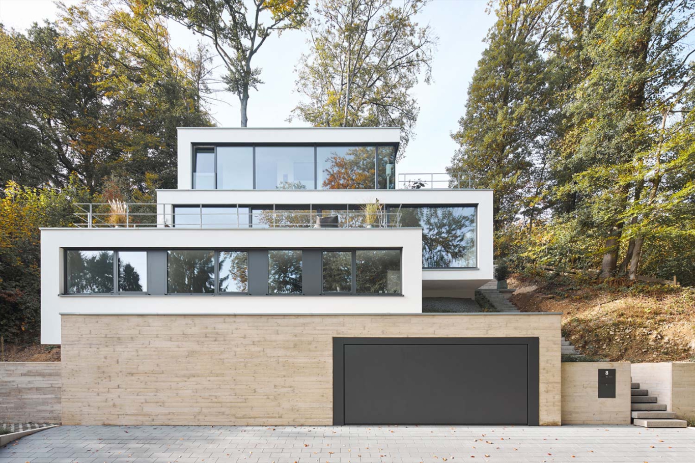 Architekturfotografie Lioba Schneider: Ein weisses Einfamilienhaus mit Flachdach und in mehreren Terrassen schmiegt sich an den Hang im Wald.