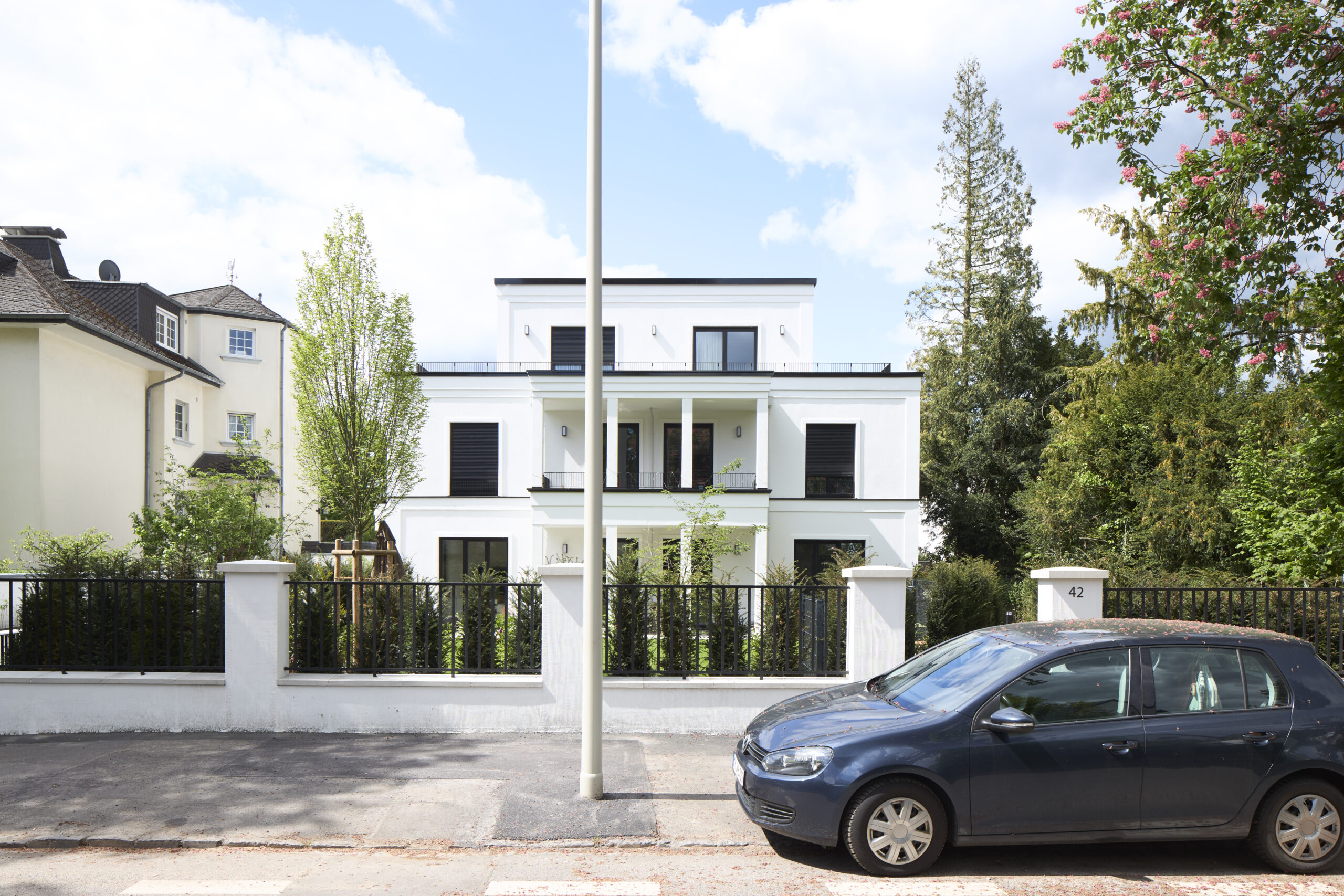 Architekturfotografie eines Mehrfamilienhauses in Bonn. Eine Aussenaufnahme zeigt ein dreistöckiges weisses elegantes MFH mit zurückspringender Attika.