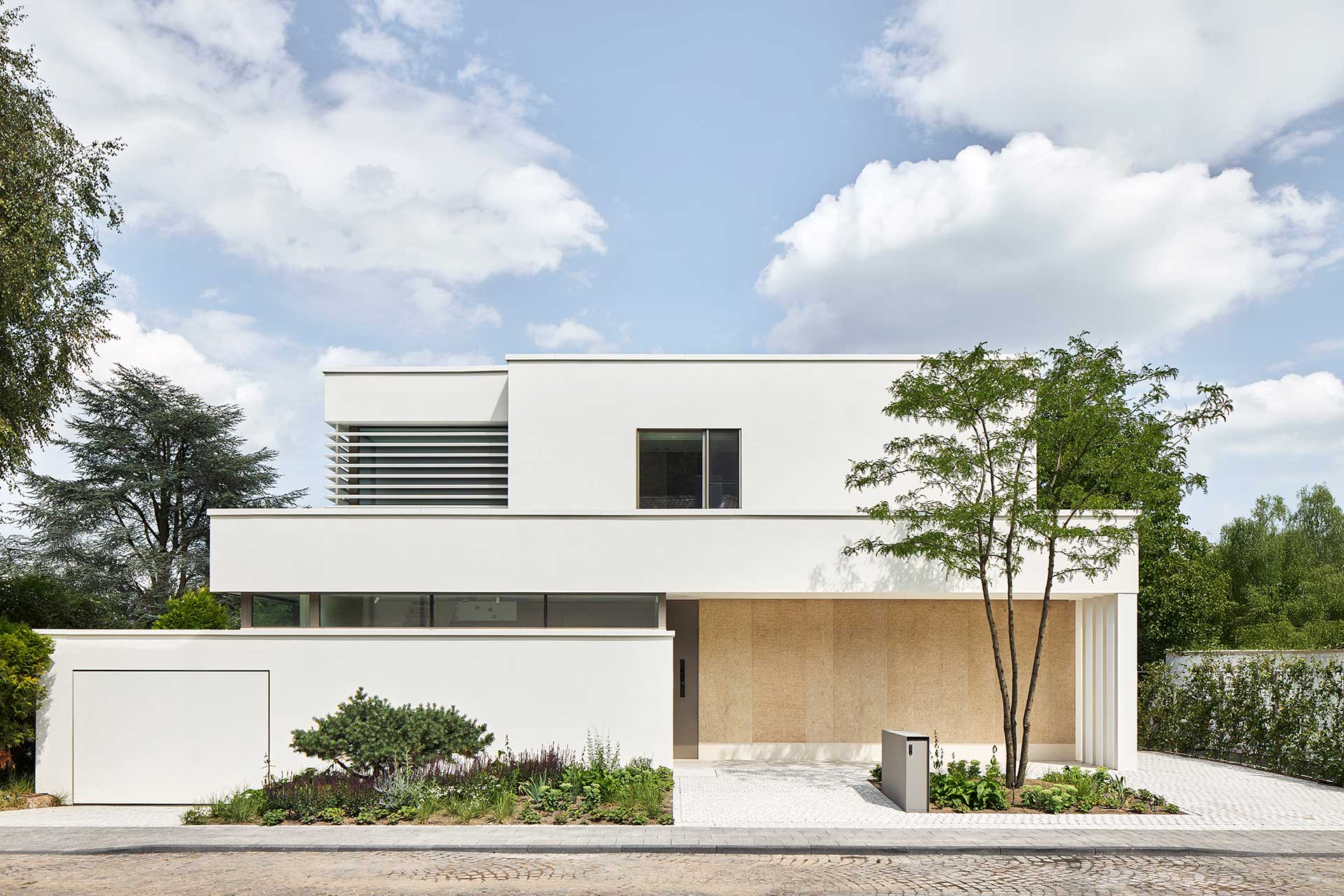 Diese Architekturfotografie zeigt ein modernes weises grosszügiges Einfamilienhaus mit grossen bodentiefen Fenstern im klassischen Stil von der Gartenseite aus.