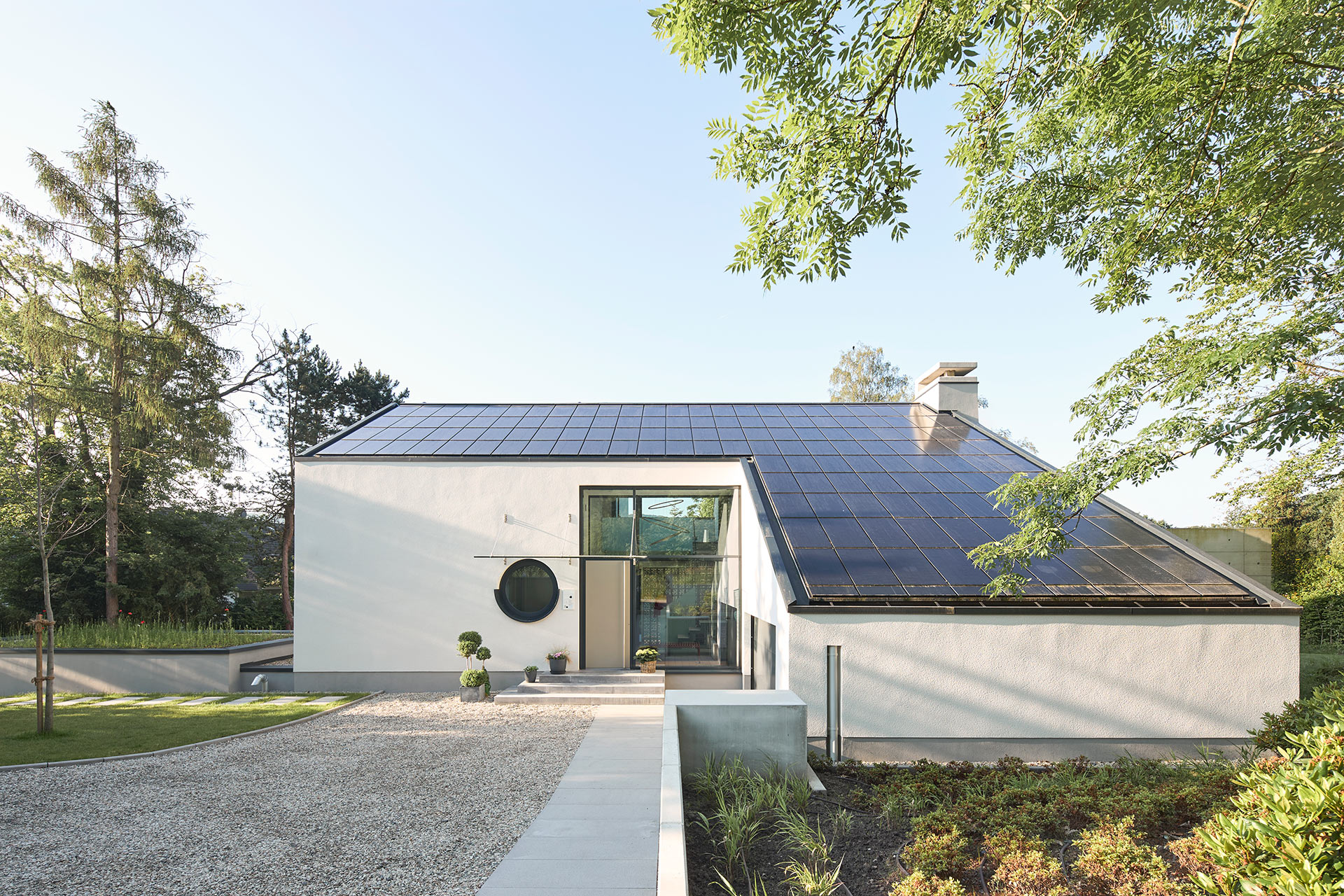 Architekturfotografie eines freistehenden Einfamilienhauses mit weissem Putz in Gevelsberg von der Eingangsseite mit Photovoltaik auf dem Dach bei Tageslicht.