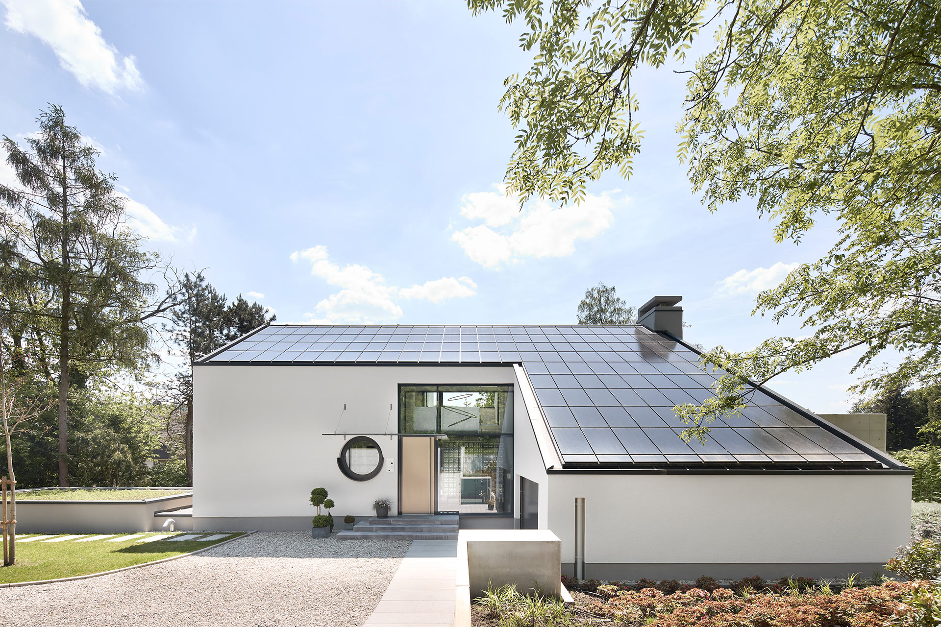 Architekturfotografie eines freistehenden Einfamilienhauses mit weissem Putz in Gevelsberg von der Eingangsseite mit Photovoltaik auf dem Dach bei Tageslicht.
