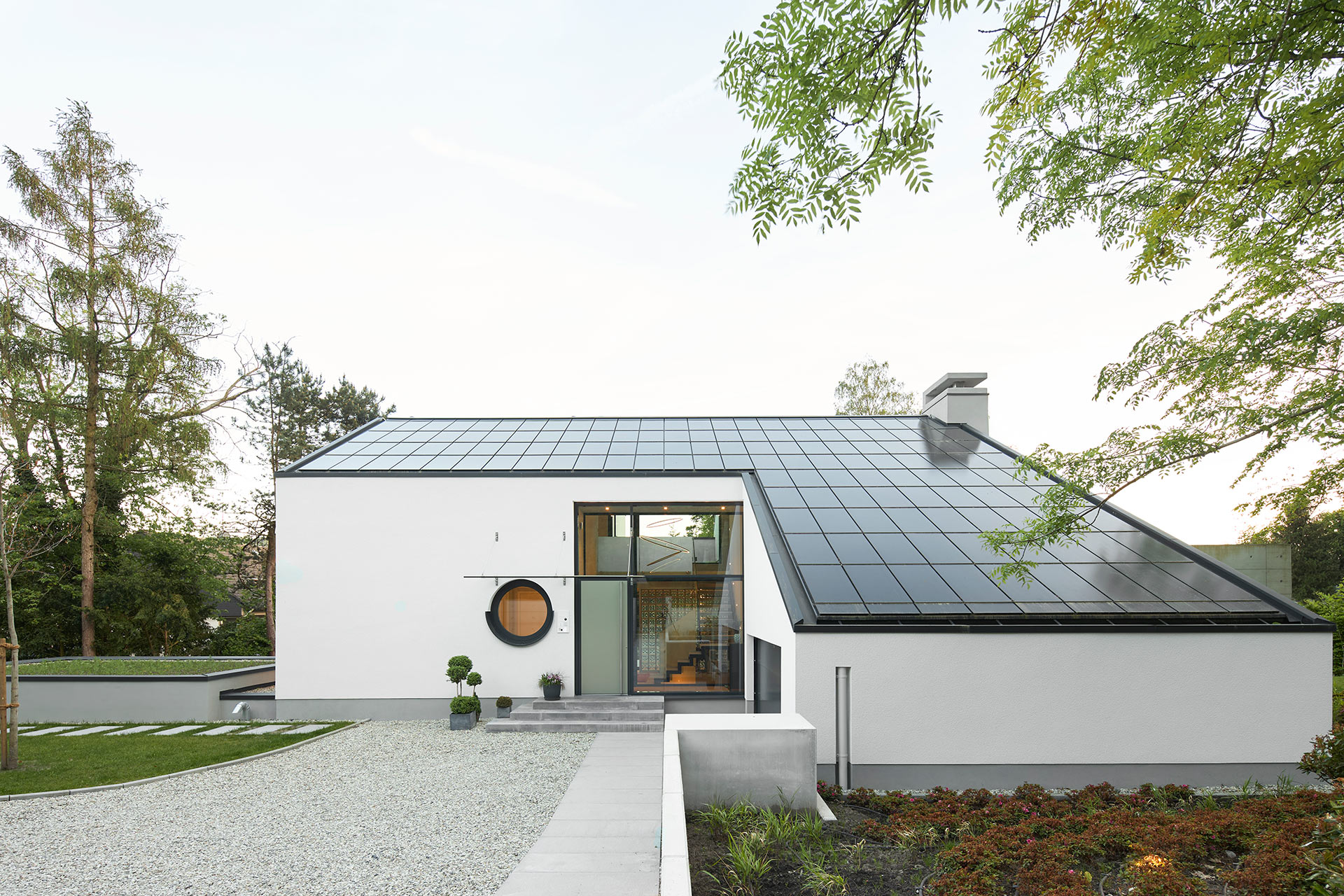 Architekturfotografie eines freistehenden Einfamilienhauses mit weissem Putz in Gevelsberg von der Eingangsseite mit Photovoltaik auf dem Dach in der Dämmerung.