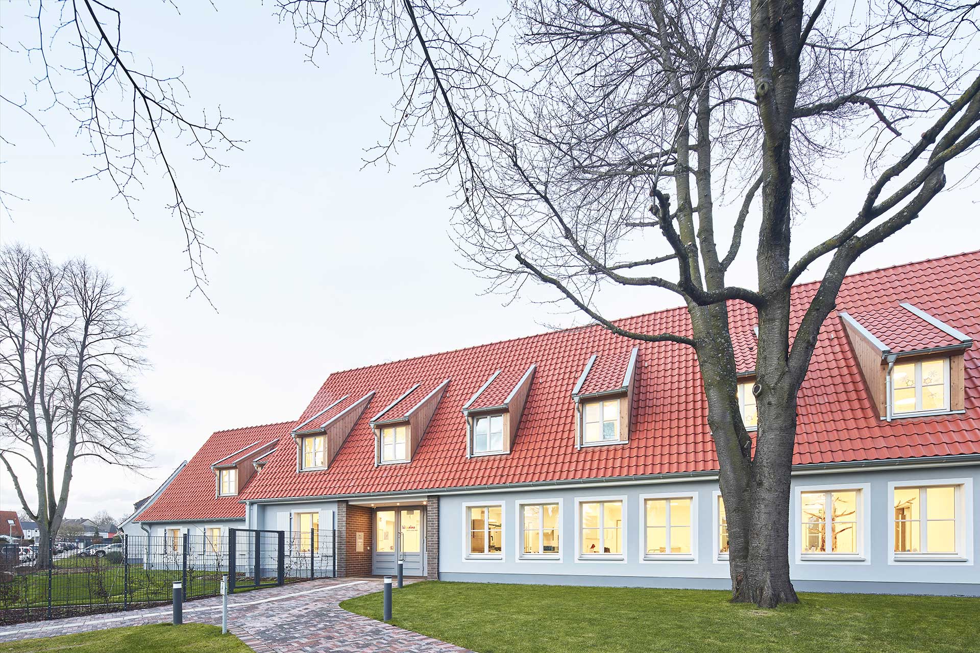 Architekturfotografie in der Dämmerung der Kita Pestalozziweg in Essen. Ein zweigeschossiger langgestreckter Bau mit Gaubenfenstern im relativ spitzen Dach.