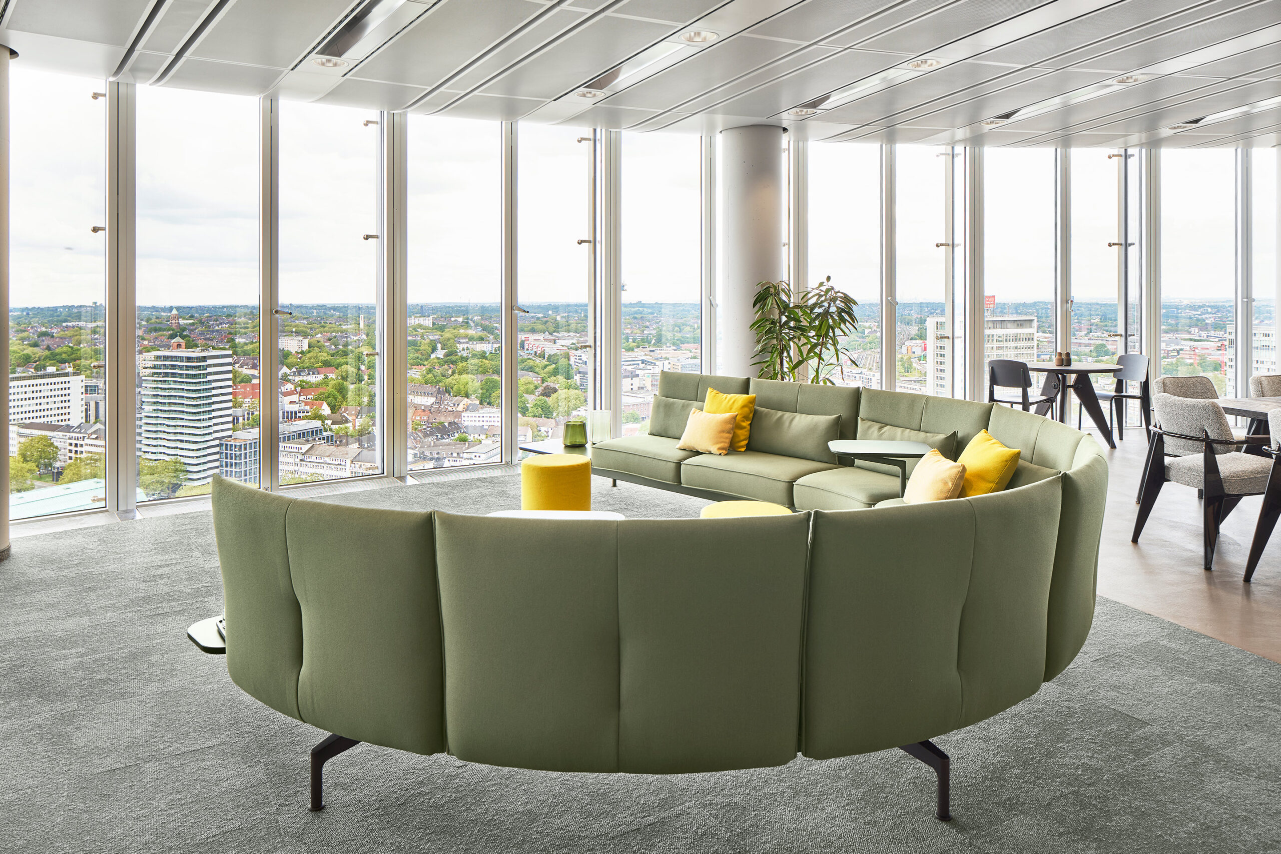Architekturfotografie eines großzügigen Büros mit bodentiefen Fenstern mit Blick aufs Ruhrgebiet, einem grünen halbrunden Sofa und weiteren modernen Möbeln der Firma Vitra– fotografiert von Lioba Schneider, Architekturfotografin.