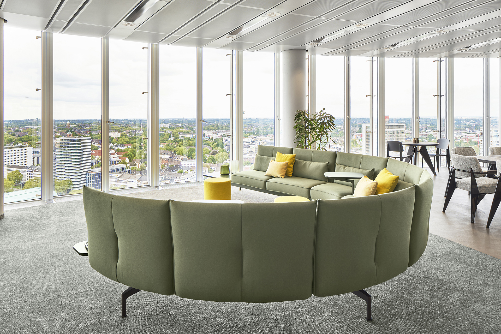 Interieurfotografie einer umgebauten Anwaltskanzlei im RWE-Turm in Essen. Bodentiefe Fenster geben den Blick frei auf das Ruhrgebiet. Ein grünes halbrundes Sofa von Vitra steht im grosszügigen Raum.