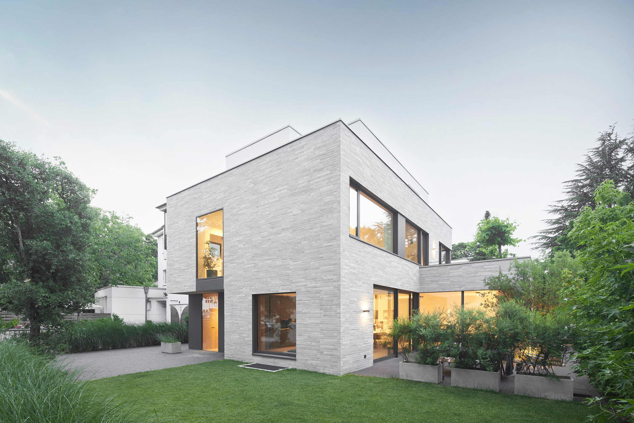 Architekturfotografie eines eleganten Einfamilienhauses in Köln mit einer Fassade aus hellem Klinker und großen Fensteröffnungen zum Garten in der Dämmerung.