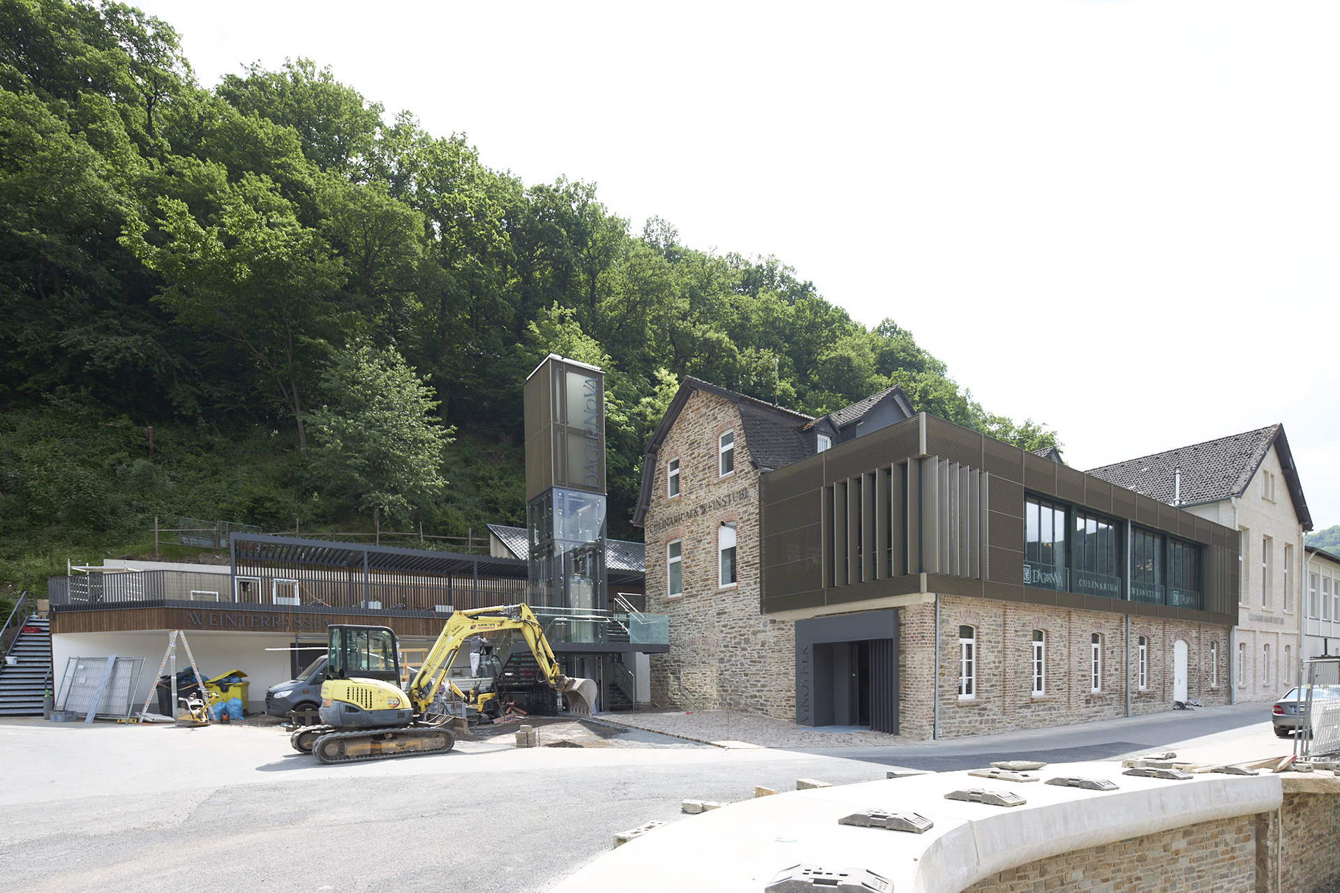 Architekturfotografie des Wiederaufbau des Weinguts der Dagernova.im Ahrtal. Ein Auf- und Anbau aus braunem Metall verbindet sich mit der alten Architektur aus Ziegelgemäuern. Auf dem Vorplatz stehen Bagger und Baugerätschaften.